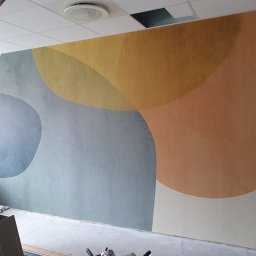 Oskar Ancypa - Ściana z abstrakcyjnym malowaniem w ciepłych i chłodnych odcieniach, widoczne drabina malarska i narzędzia, sugerujące prace wykończeniowe w pomieszczeniu.