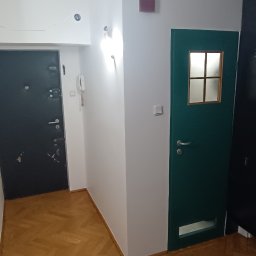 Remonty Na Poziomie Filip Kitliński Usługi Wykończeniowo-Remontowe - Korytarz po remoncie: świeżo pomalowane ściany na biało, odnowione drzwi wejściowe i wewnętrzne, parkiet po renowacji. Widok na wykończone wnętrze.