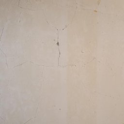 Remonty Na Poziomie Filip Kitliński Usługi Wykończeniowo-Remontowe - Ściana w odcieniach beżu z widocznymi pęknięciami i ubytkami tynku, fragment włącznika światła w prawym dolnym rogu. Stan 'przed' remontem.