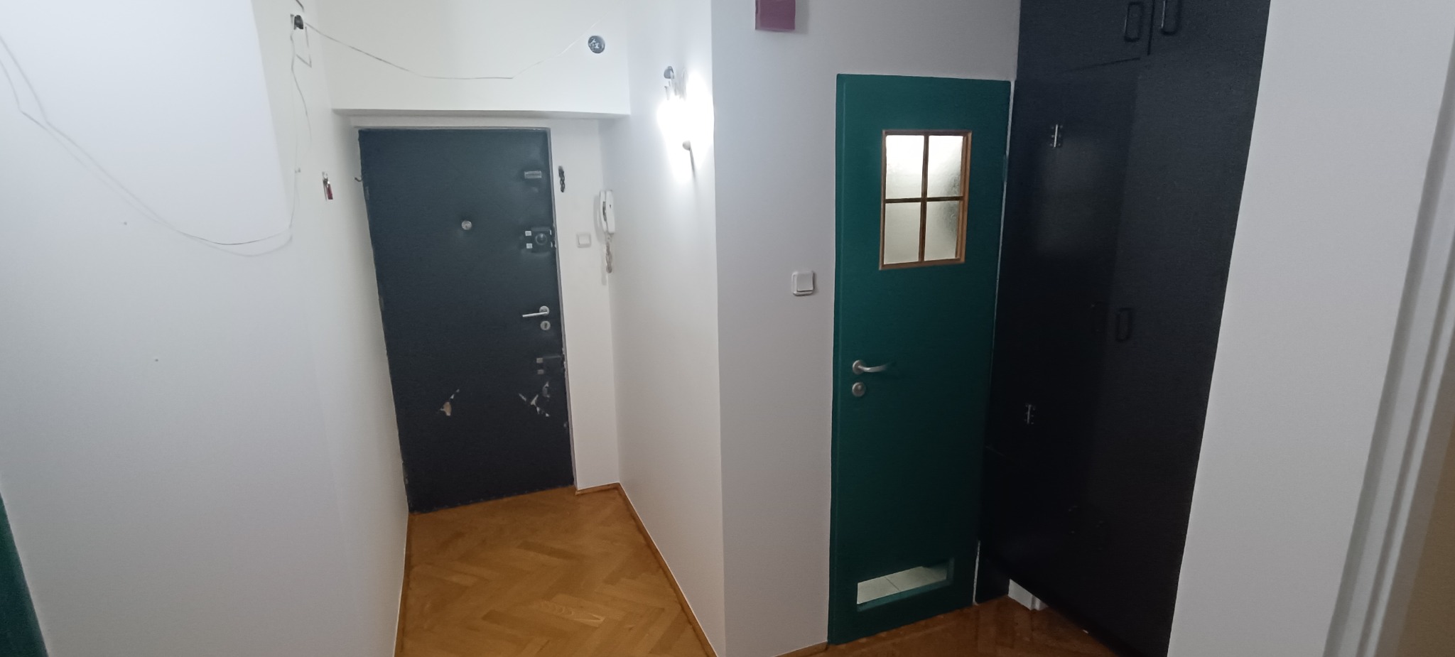 Korytarz po remoncie: świeżo pomalowane ściany na biało, odnowione drzwi wejściowe i wewnętrzne, parkiet po renowacji. Widok na wykończone wnętrze.