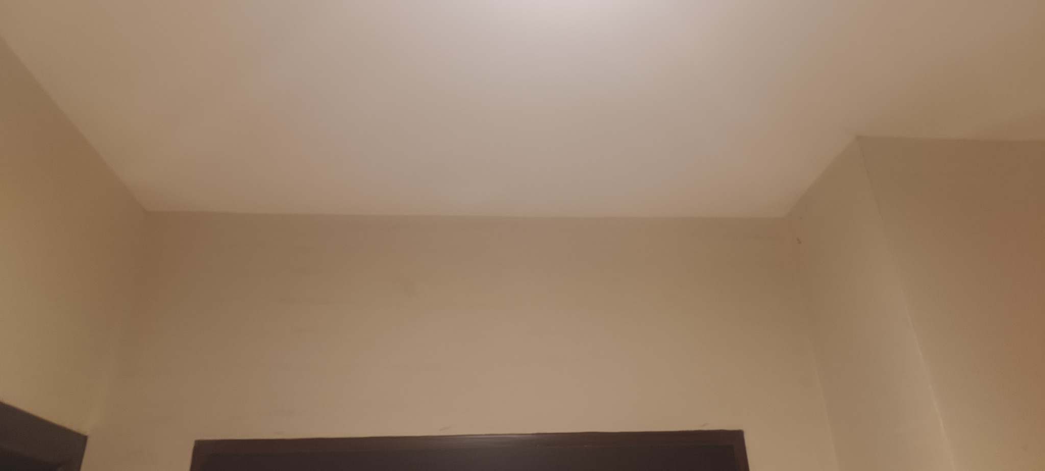 Gładki, beżowy sufit i ściana po naprawie dziur, widoczne z dołu, z fragmentem ciemnej futryny drzwi. Świeżo pomalowane, bez widocznych niedoskonałości.