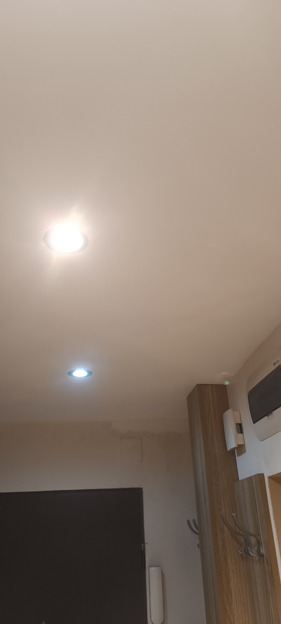 Fragment sufitu podwieszanego z dwoma punktami świetlnymi, widoczne ślady po naprawie dziur, świeżo położona gładź i pomalowane miejsce po łataniu.