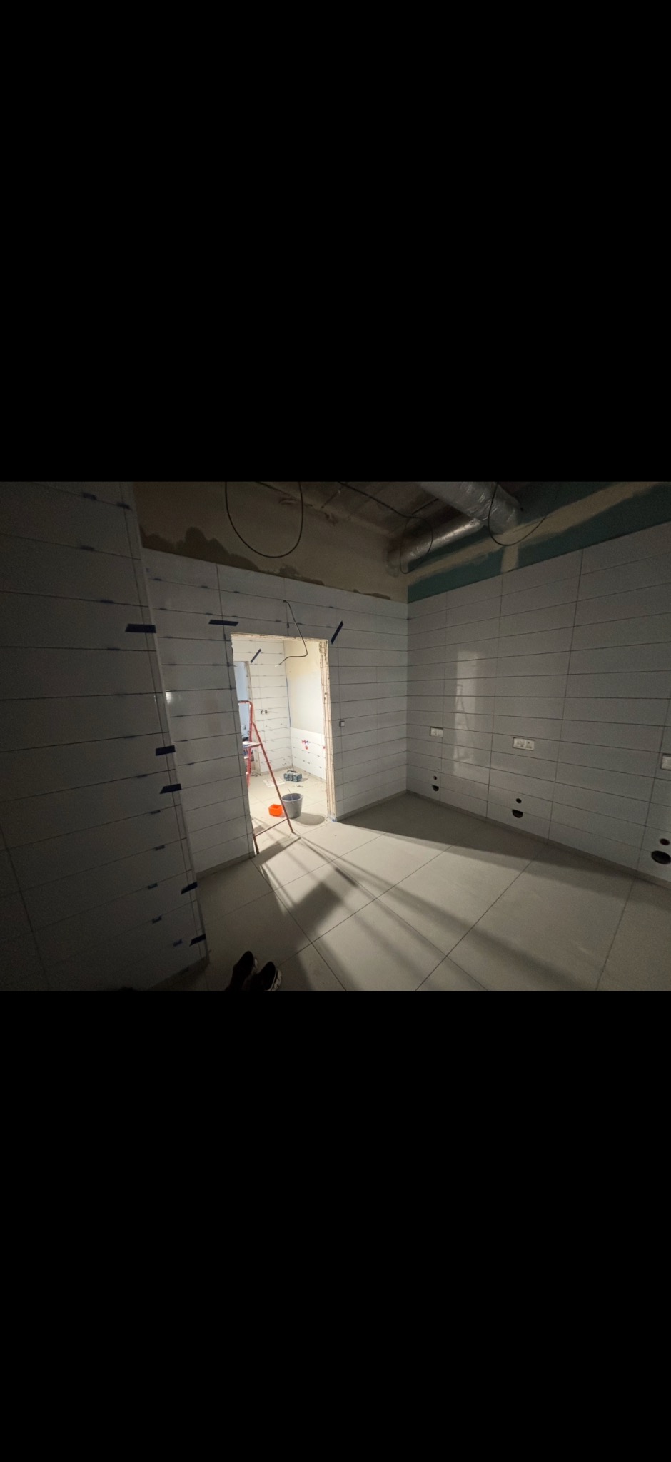 Remont łazienki w trakcie: ułożone białe płytki na ścianach z zachowaniem fug, widoczne narzędzia i drabina w tle. Etap wykończeniowy, widok z dołu.