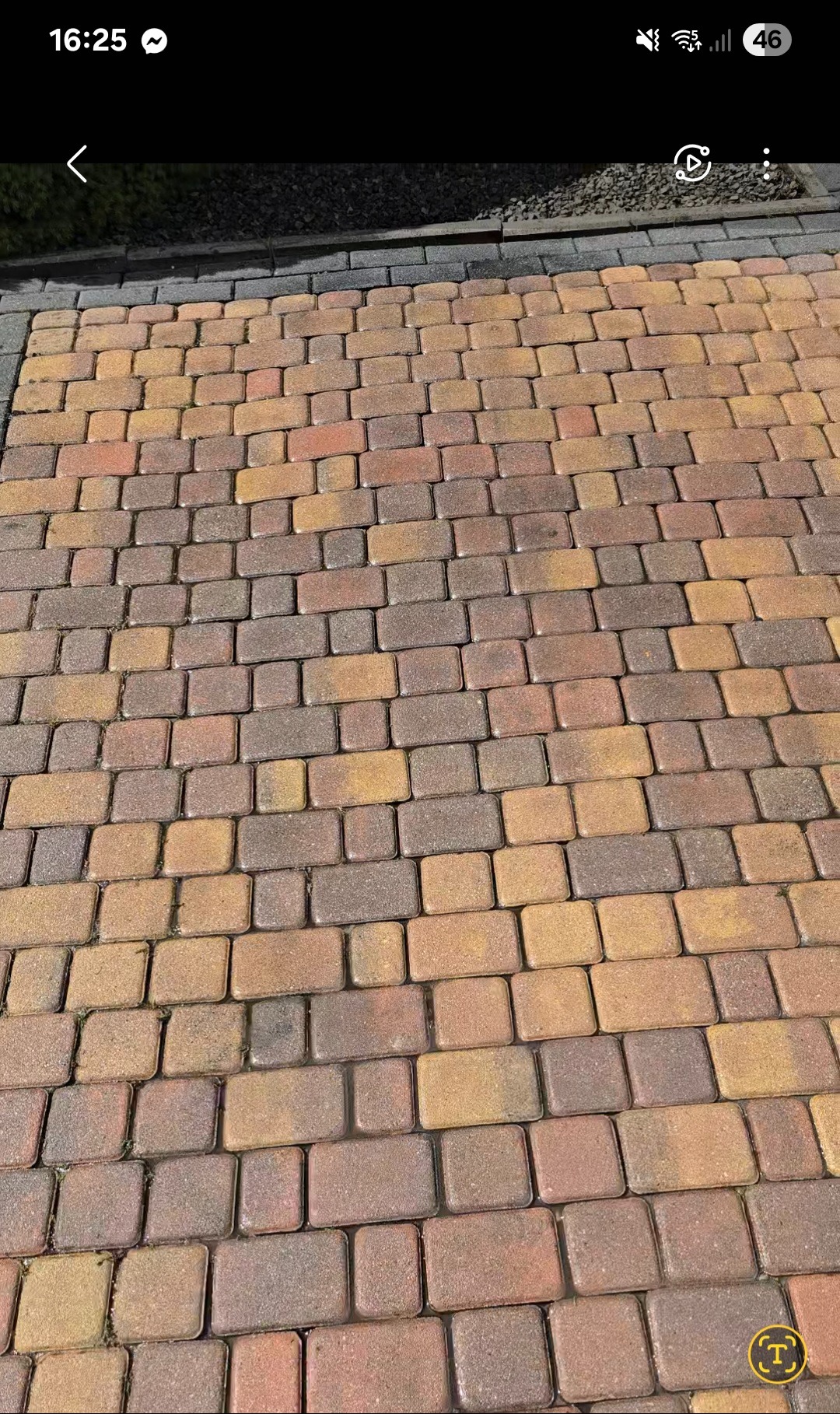 Ułożona kostka brukowa w odcieniach brązu i beżu, tworząca wzór na podjeździe. Widoczne fugi i krawędź z drobnym żwirem.