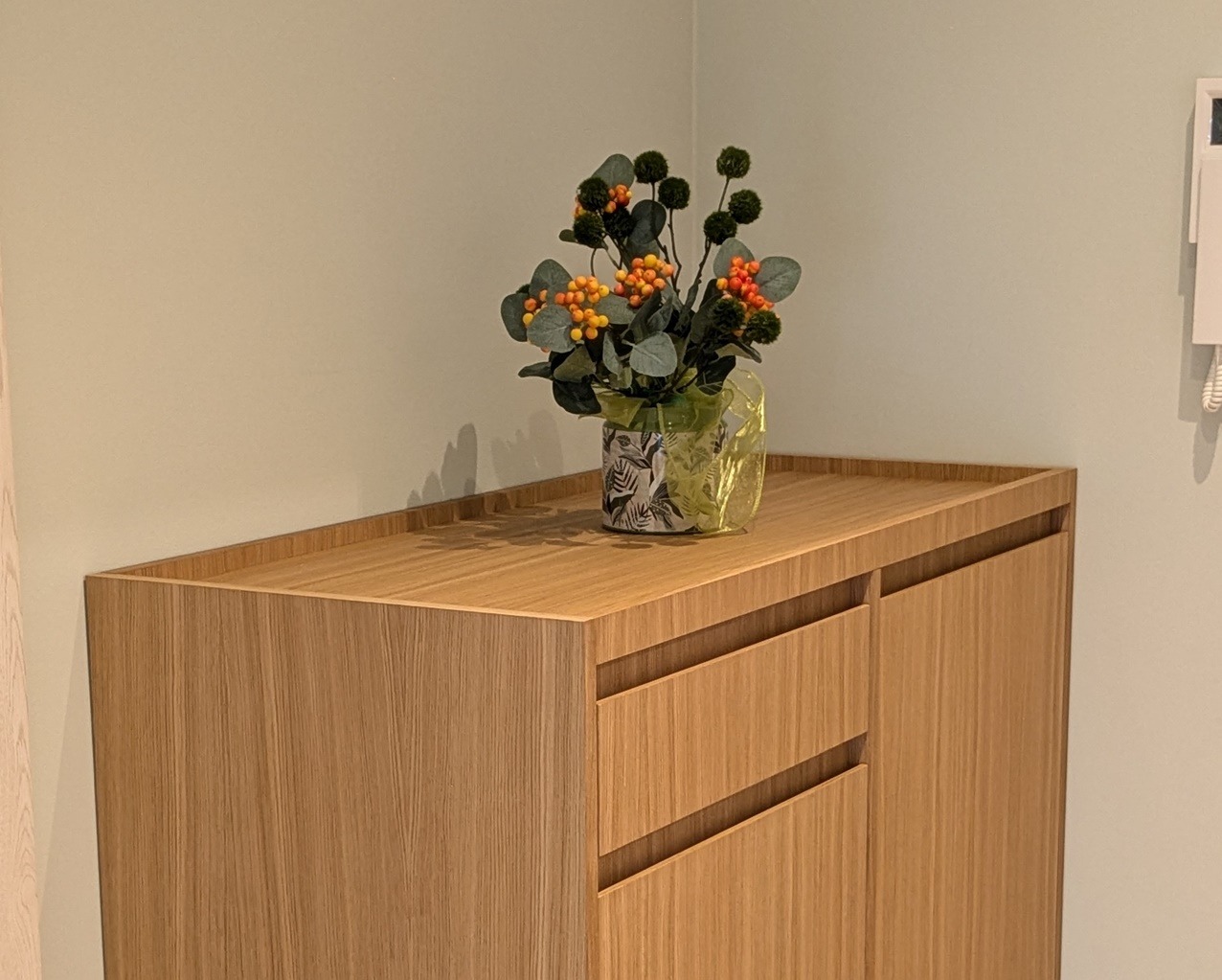 Nowoczesna szafka z drewna z dekoracyjnym wazonem na blacie. Minimalistyczny design, ciepłe oświetlenie, widoczne usłojenie drewna.