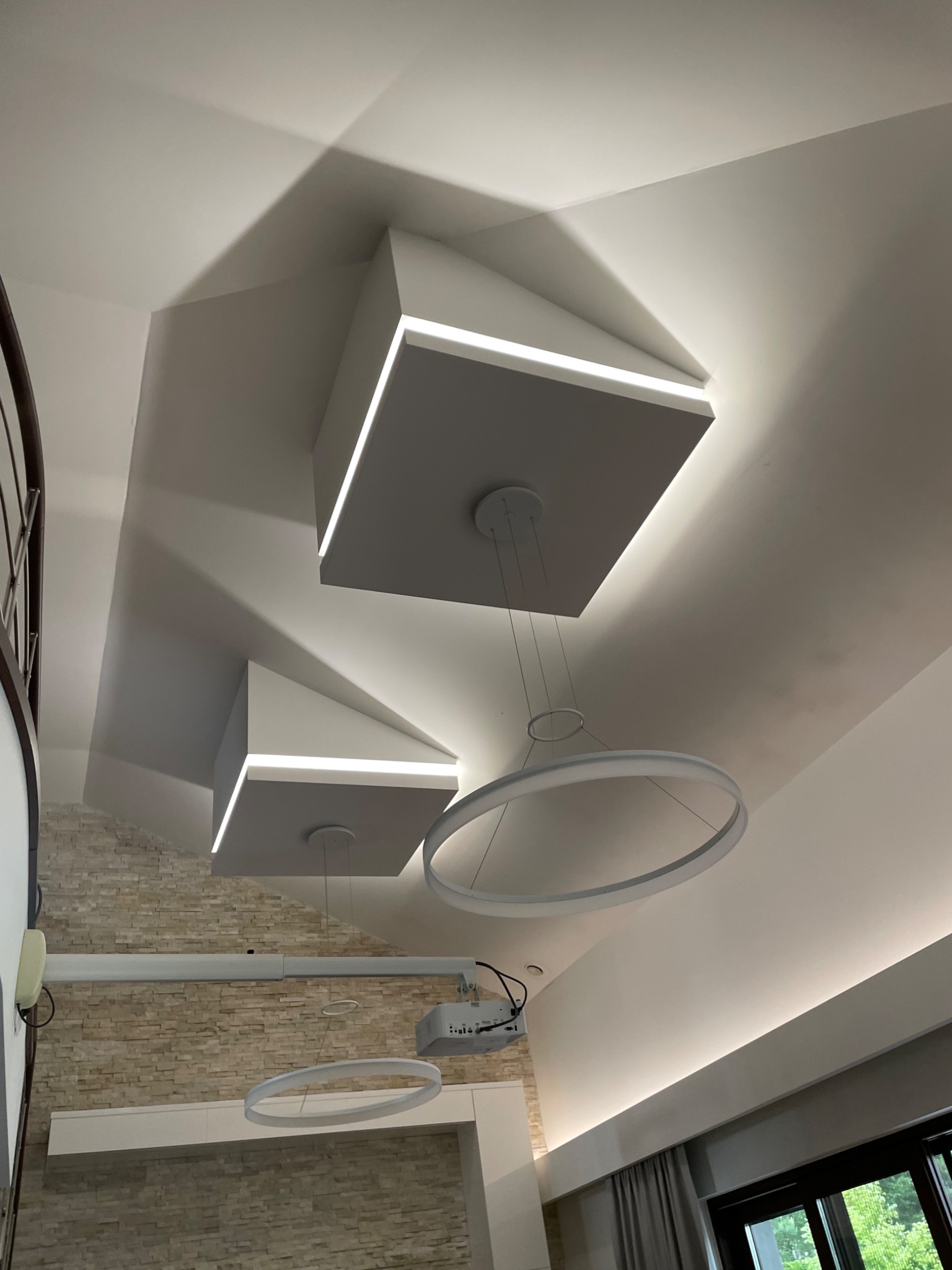 Nowoczesne oświetlenie sufitowe z geometrycznymi panelami i okrągłymi lampami wiszącymi, w jasnym wnętrzu.