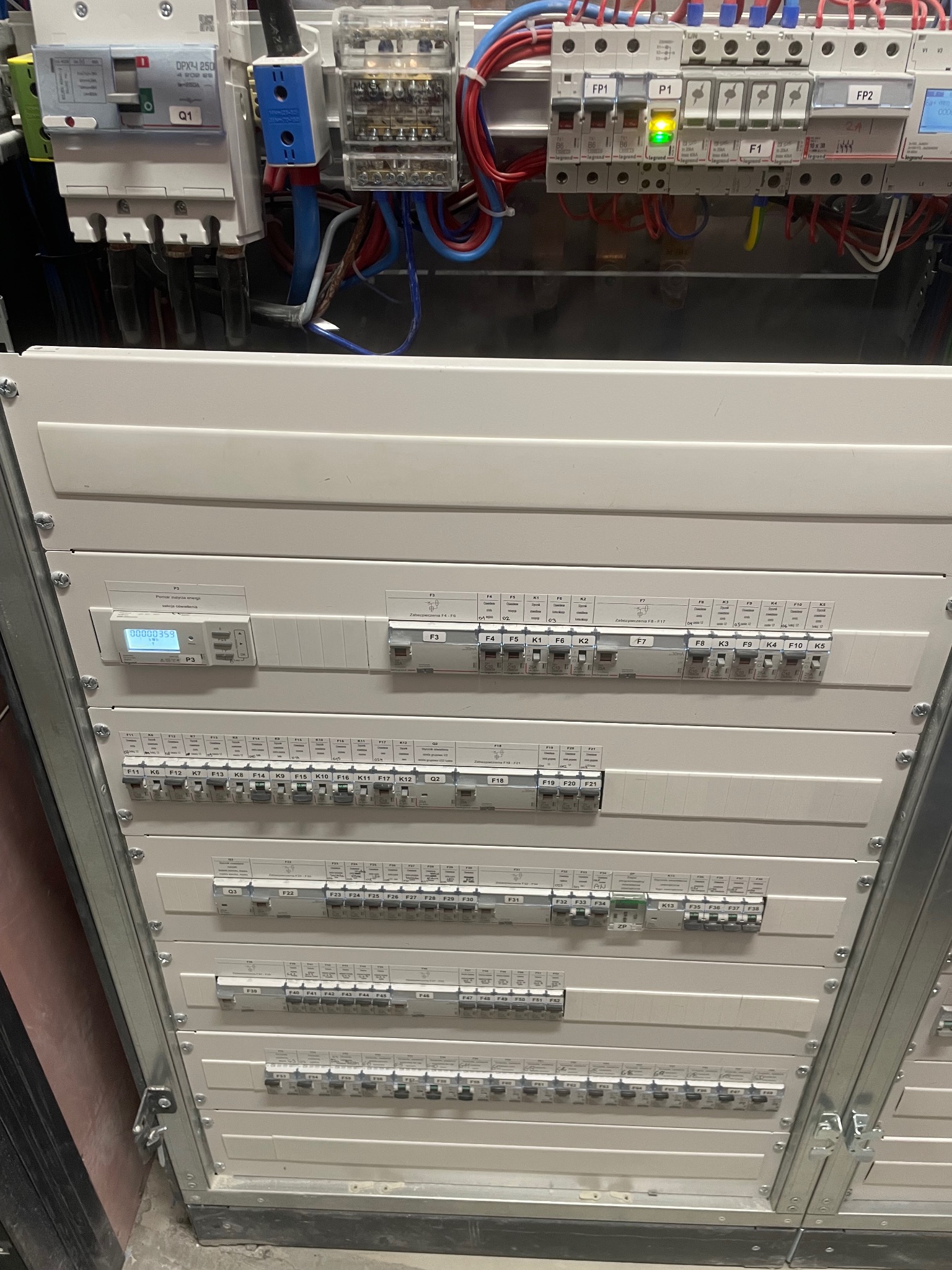 Rozdzielnia elektryczna z bezpiecznikami, okablowaniem i licznikiem zużycia energii, widok od dołu, oświetlenie górne.