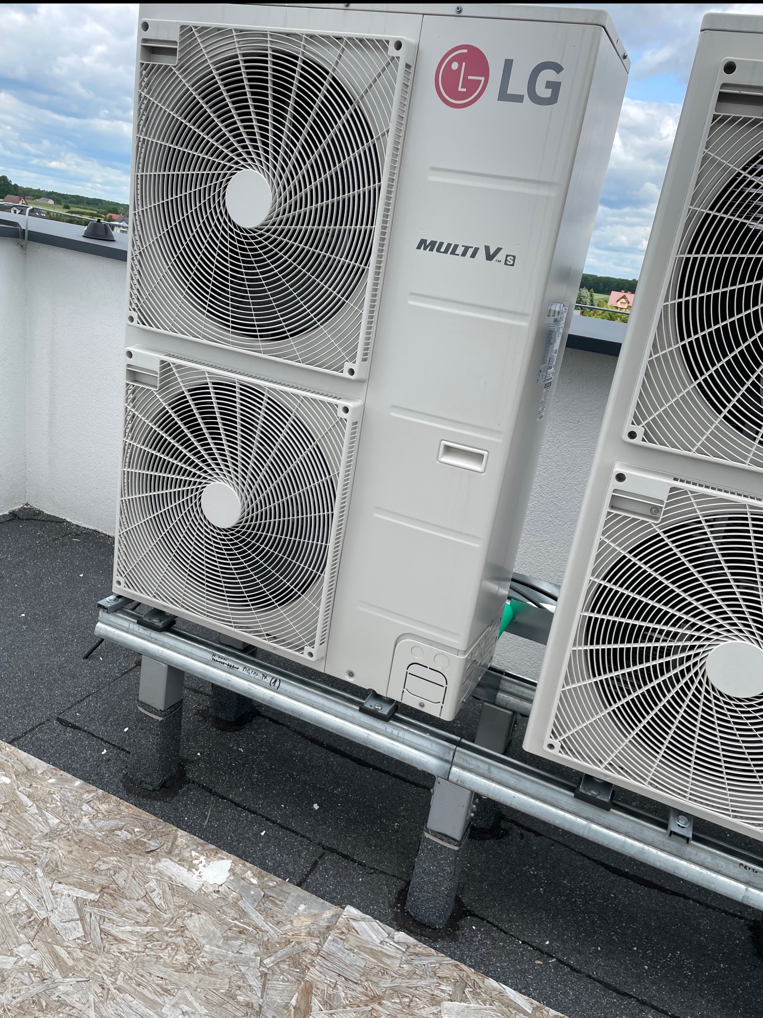 Zewnętrzne jednostki klimatyzacji LG Multi V 8 na dachu budynku, widoczne wentylatory i elementy montażowe. Tło stanowią budynki i niebo.