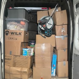 Mrówka Trans - Wnętrze białego busa wypełnione po brzegi kartonowymi pudłami (m.in. 'WILK', 'Kinderkraft'), plastikowymi pojemnikami, wężem ogrodowym Gardena i oponami.