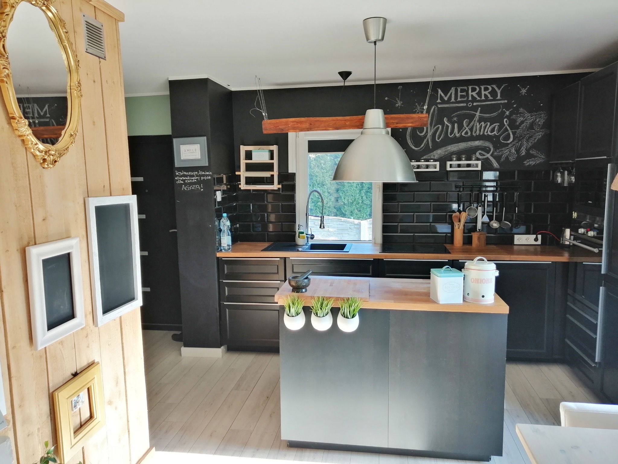 Nowoczesna kuchnia w Brzuśniku z czarnymi frontami, drewnianym blatem i tablicą kredową z świątecznym motywem. Uwagę zwraca wyspa kuchenna z ziołami.