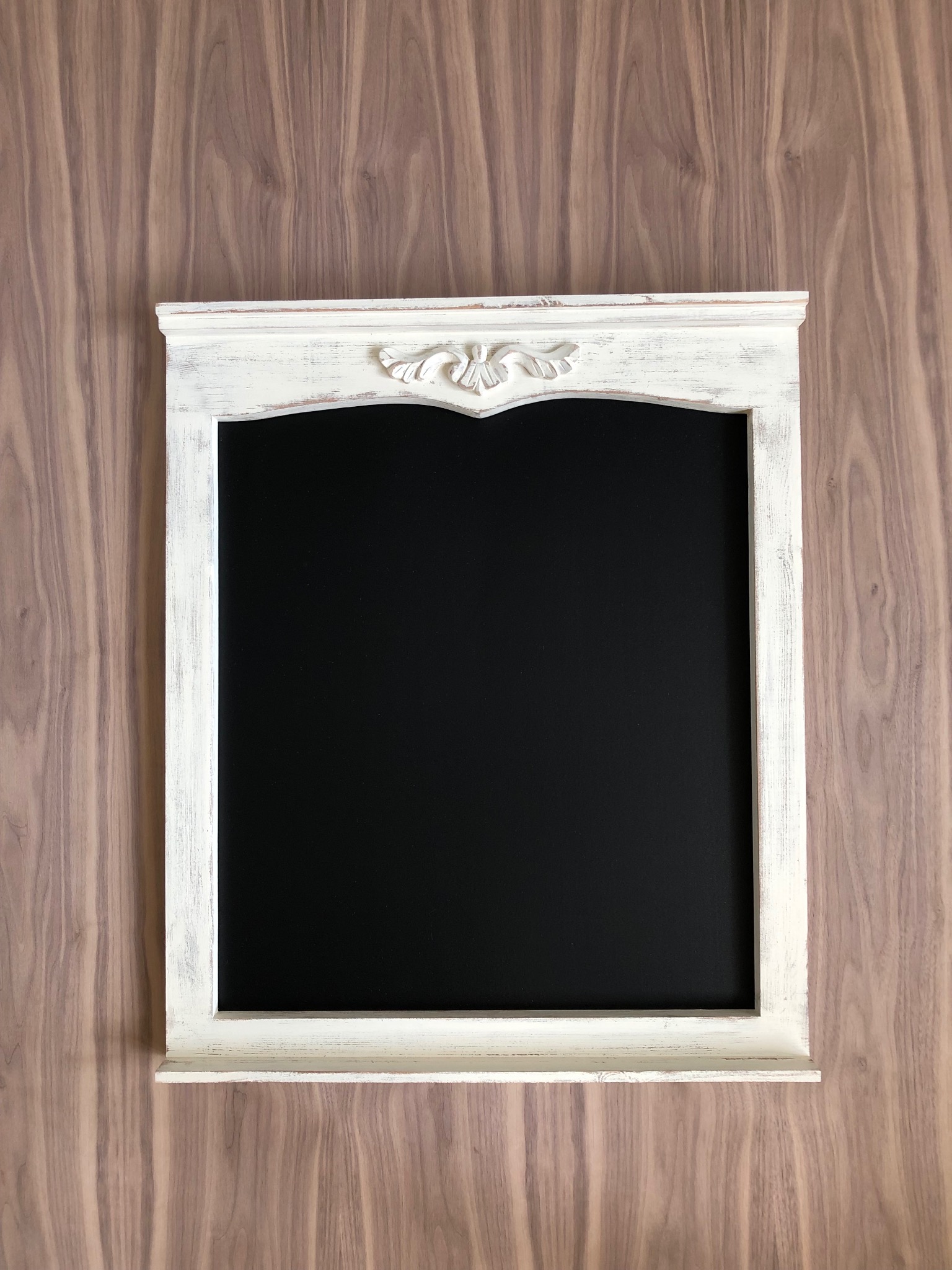 Rustykalna, biała rama lustra z dekoracyjnym ornamentem, zawieszona na ścianie z drewnianą okładziną. Czarne lustro. Styl vintage, bliski kadr.