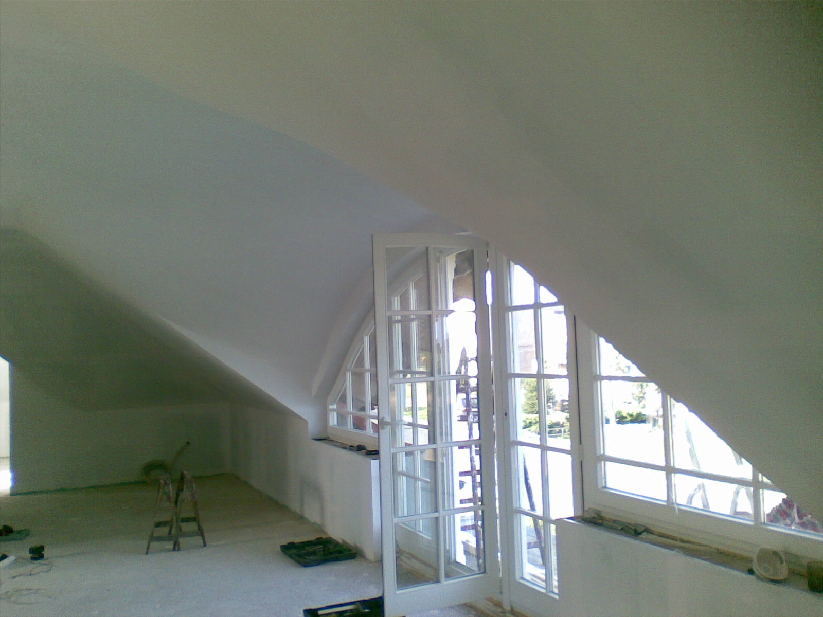 Poddasze ze skośnym sufitem i oknami, ściany po szpachlowaniu, przygotowane do malowania, widoczne narzędzia malarskie i drabina.