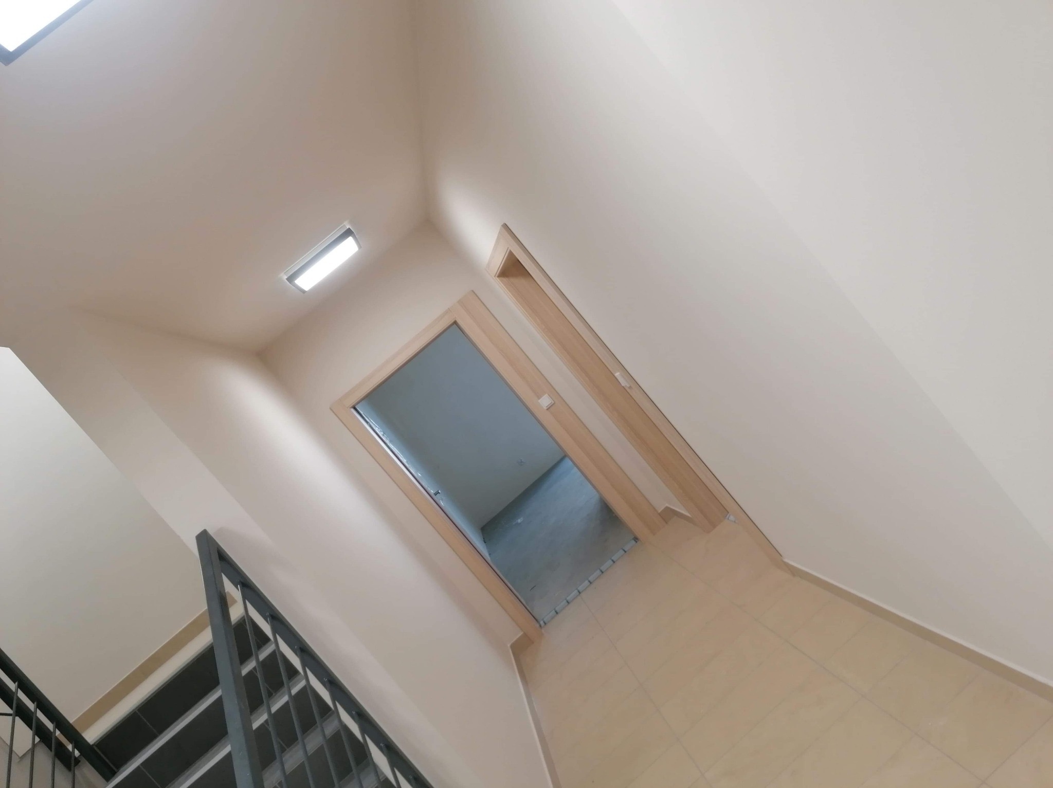 Jasne wnętrze klatki schodowej po remoncie: świeżo pomalowane ściany w odcieniach beżu, płytki podłogowe i metalowa balustrada. Widok z góry na otwarte drzwi.