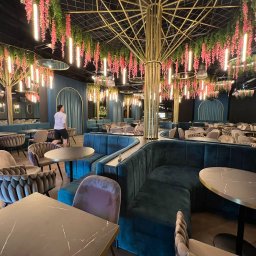 ELEKTROINVEST Sp. z o.o. - Wnętrze restauracji z dekoracyjnym oświetleniem: wiszące kwiaty i pionowe lampy tworzą unikalny klimat. Turkusowe sofy i marmurowe stoliki.