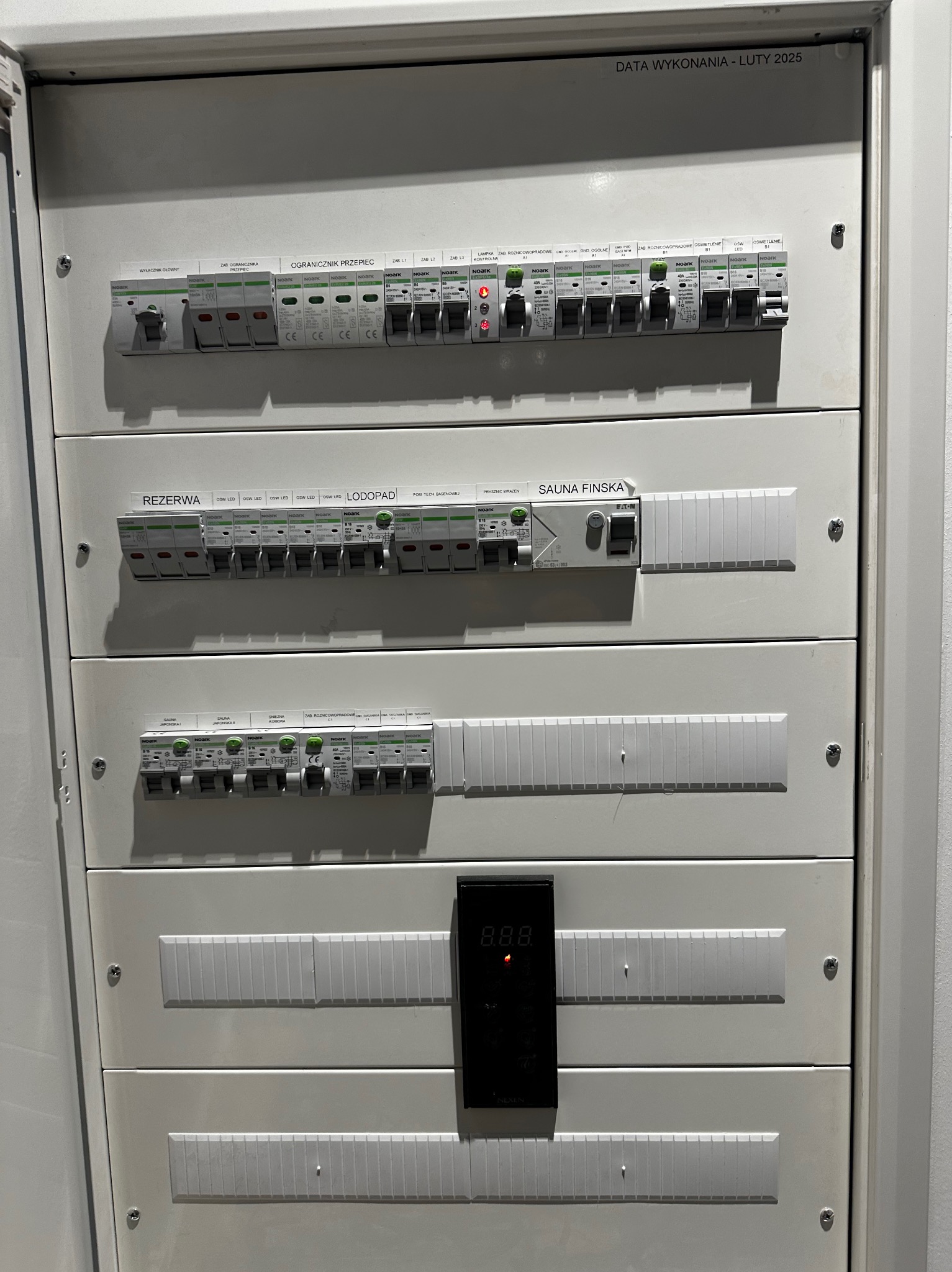 Rozdzielnica elektryczna z wyłącznikami, opisana sekcjami: 'Ogranicznik przepięć', 'Rezerwa', 'Sauna Fińska', z datą wykonania Luty 2025.