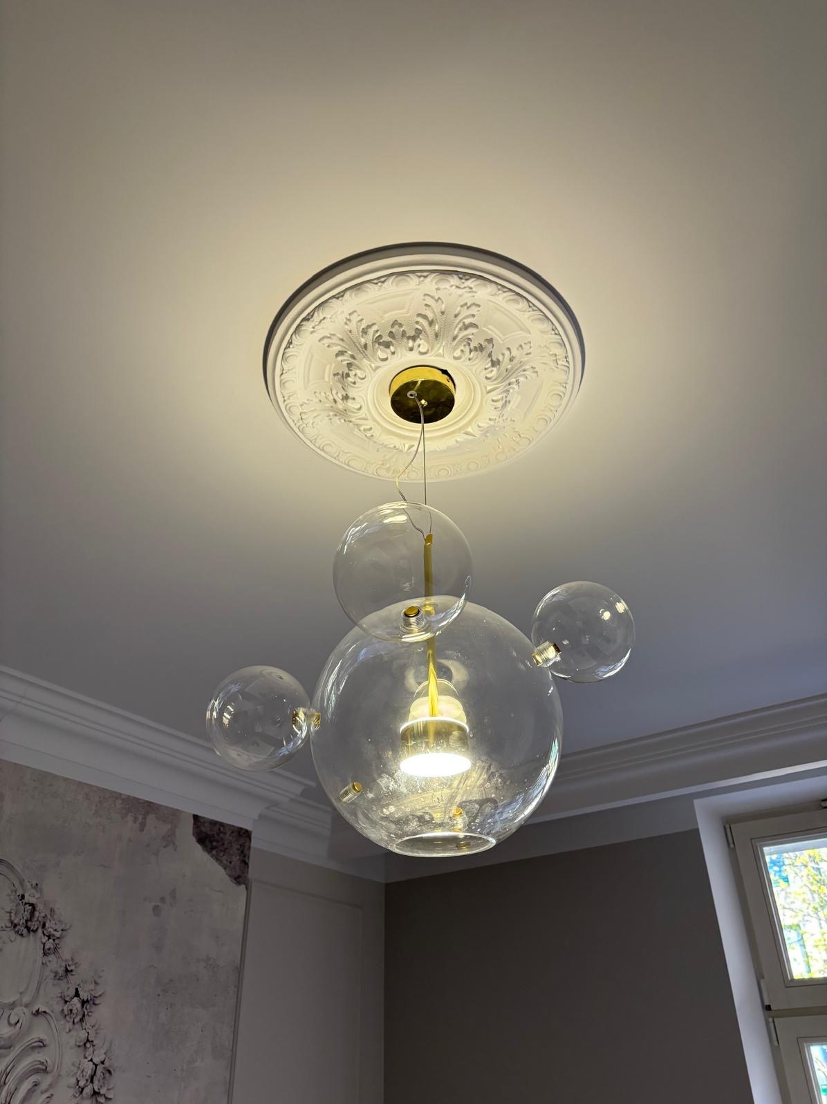 Szklana lampa sufitowa w stylu bubble z dekoracyjną rozetą sufitową, widok od dołu, ciepłe światło żarówki, nowoczesny design.