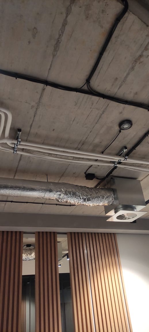 Betonowy sufit z widocznymi instalacjami elektrycznymi: czarne i białe kable, oświetlenie punktowe oraz fragment instalacji wentylacyjnej. Widok z dołu.