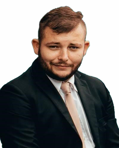 Portret mężczyzny z brodą w czarnym garniturze i jasnym krawacie, uśmiechającego się do kamery na jednolitym tle. Profesjonalny wizerunek, potencjalnie dla firmy.