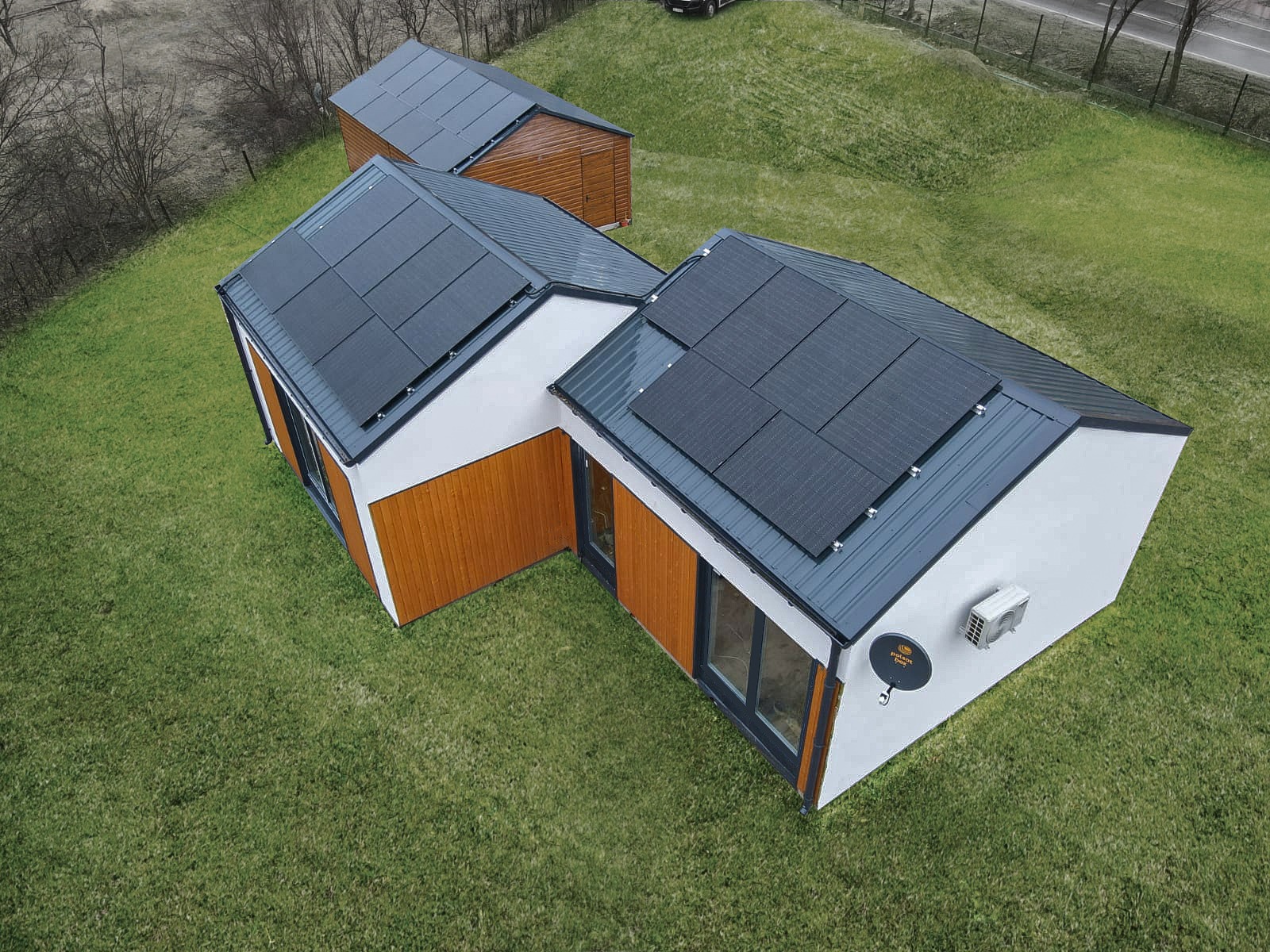 Nowoczesny dom szkieletowy z panelami solarnymi na dachu, widok z góry na zielonym trawniku. Białe ściany i drewniana elewacja, antena satelitarna na ścianie.