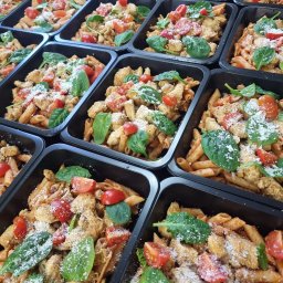 Poezja Smaku Catering - Penne z kurczakiem, pomidorami, szpinakiem i parmezanem w czarnych pojemnikach. Gotowe porcje cateringu dietetycznego ułożone rzędami.