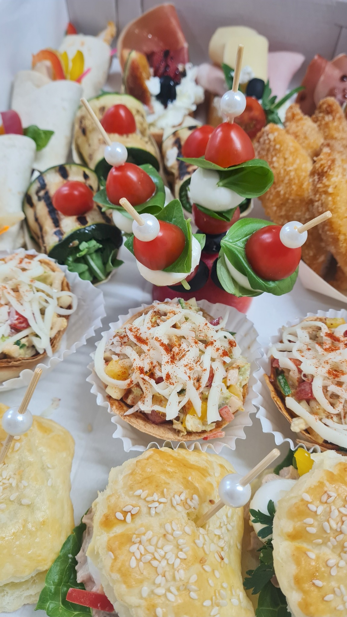 Ekskluzywny zestaw przekąsek: mini tartaletki z sałatką, koreczki z pomidorkami i mozzarellą, grillowana cukinia i mini kanapki z sezamem, idealne na elegancki catering.