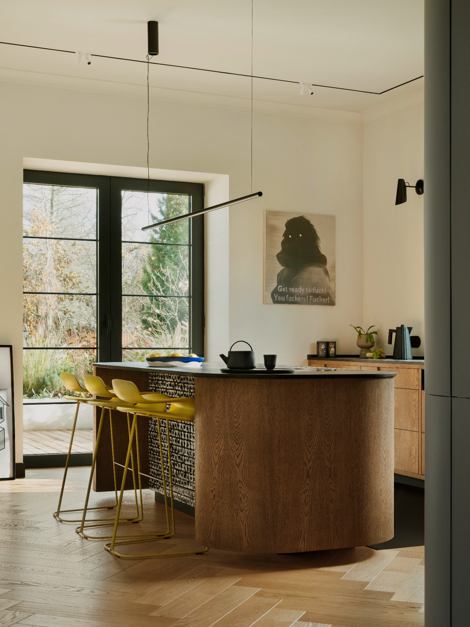 Nowoczesna kuchnia z wyspą i żółtymi krzesłami barowymi w Konstantynowie Łódzkim. Parkiet w jodełkę, czarne okno z widokiem na zieleń. Minimalistyczny design.