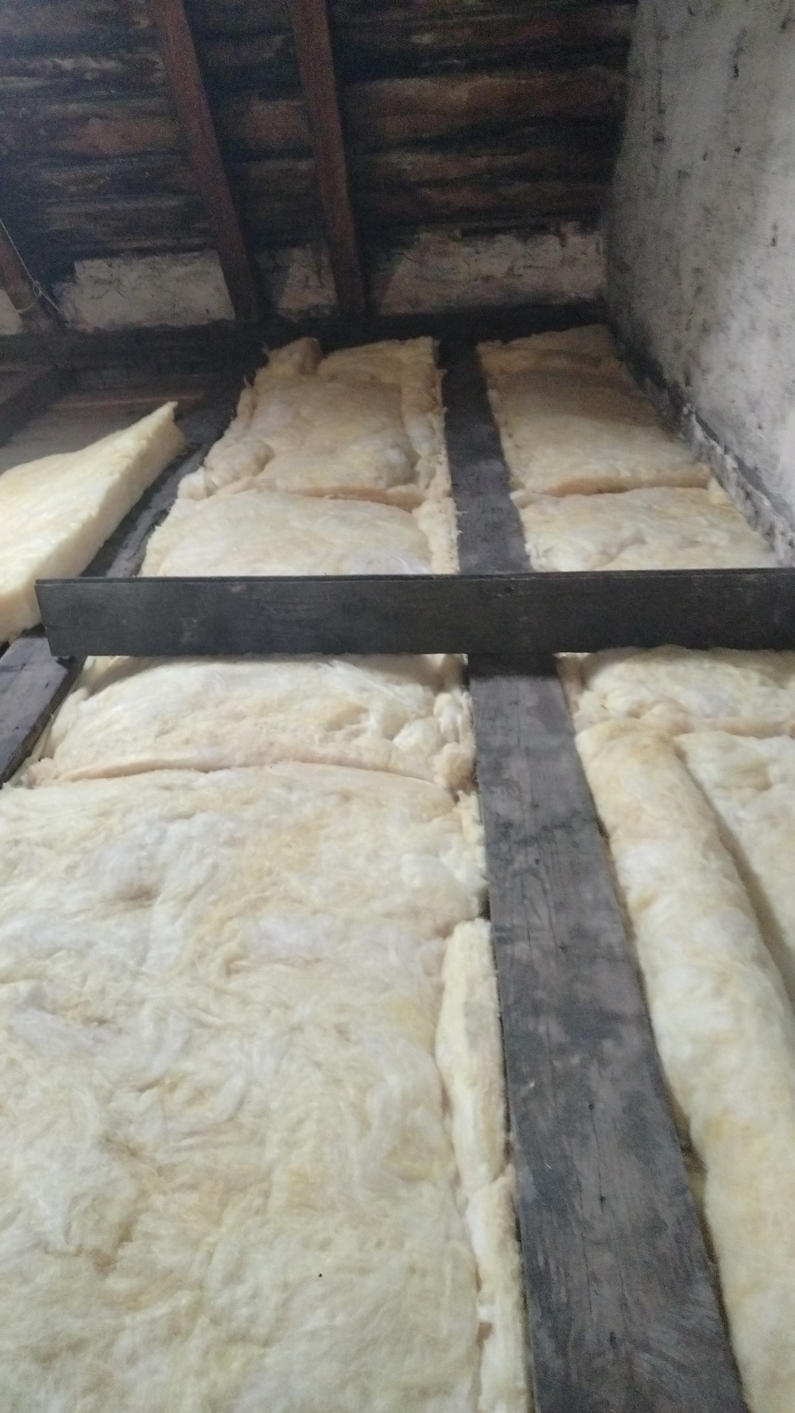 Ocieplenie poddasza wełną mineralną, widoczne drewniane belki konstrukcyjne i warstwa izolacyjna, surowy stan przed wykończeniem.