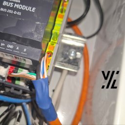 Magazyn Energii - Inteligentne Domy - Elektryka - VoltLogic - Detale połączeń modułu BUS-201-D-01 z kolorowymi przewodami w skrzynce rozdzielczej. Widoczne złącza V+, GND, A, B oraz zabezpieczone kable.