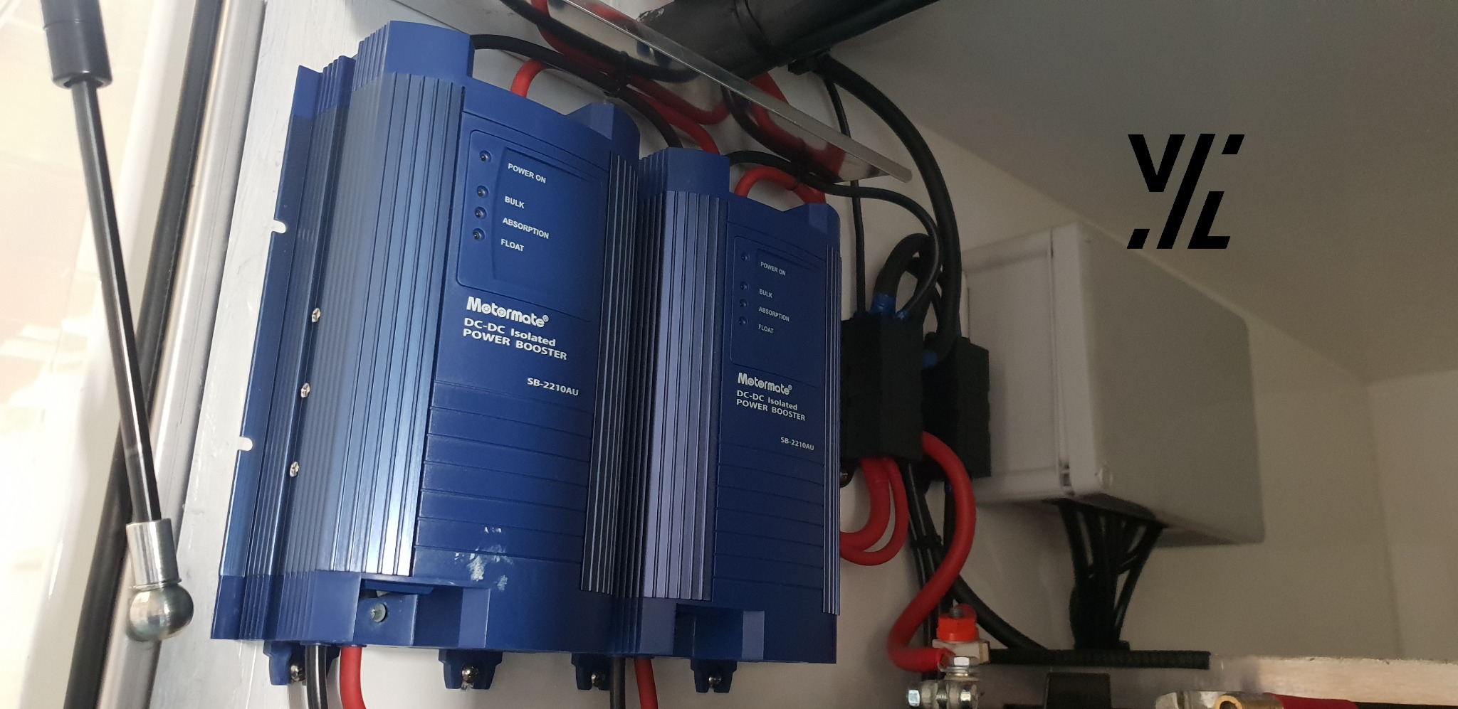 Dwa niebieskie izolowane wzmacniacze mocy DC-DC Metermate SB-2210AU z okablowaniem wewnątrz białej szafki. Widoczne diody LED, złącza i przewody.