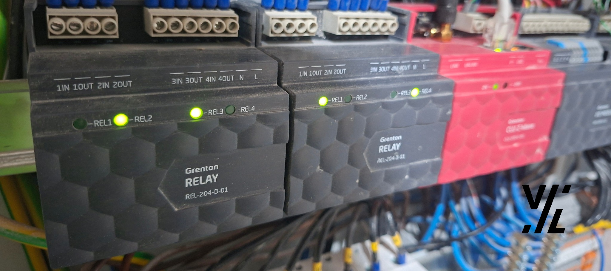Szczegółowe ujęcie szyny DIN z modułami Grenton Relay REL-204-D-01. Widoczne diody LED sygnalizujące stan przekaźników oraz złącza wejść/wyjść. Okablowanie w tle.