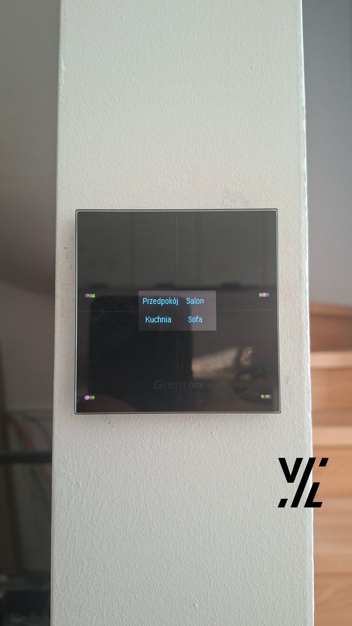 Panel sterowania inteligentnego domu firmy Grenton, zamontowany na ścianie. Wyświetlacz pokazuje opcje sterowania oświetleniem w różnych pomieszczeniach.