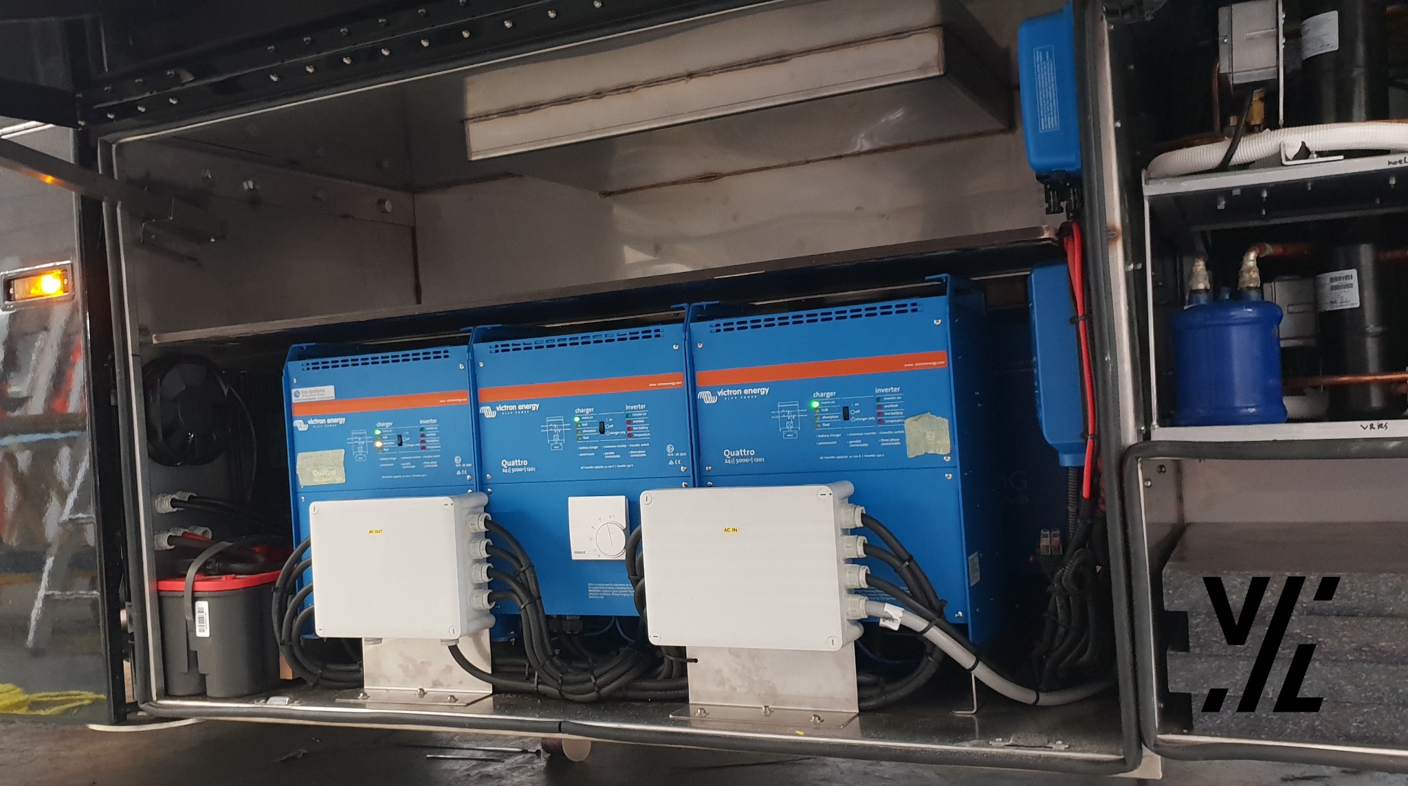 Instalacja magazynu energii: trzy niebieskie inwertery Victron Quattro z białymi skrzynkami przyłączeniowymi w metalowej szafie. Widoczne przewody i dodatkowe komponenty.