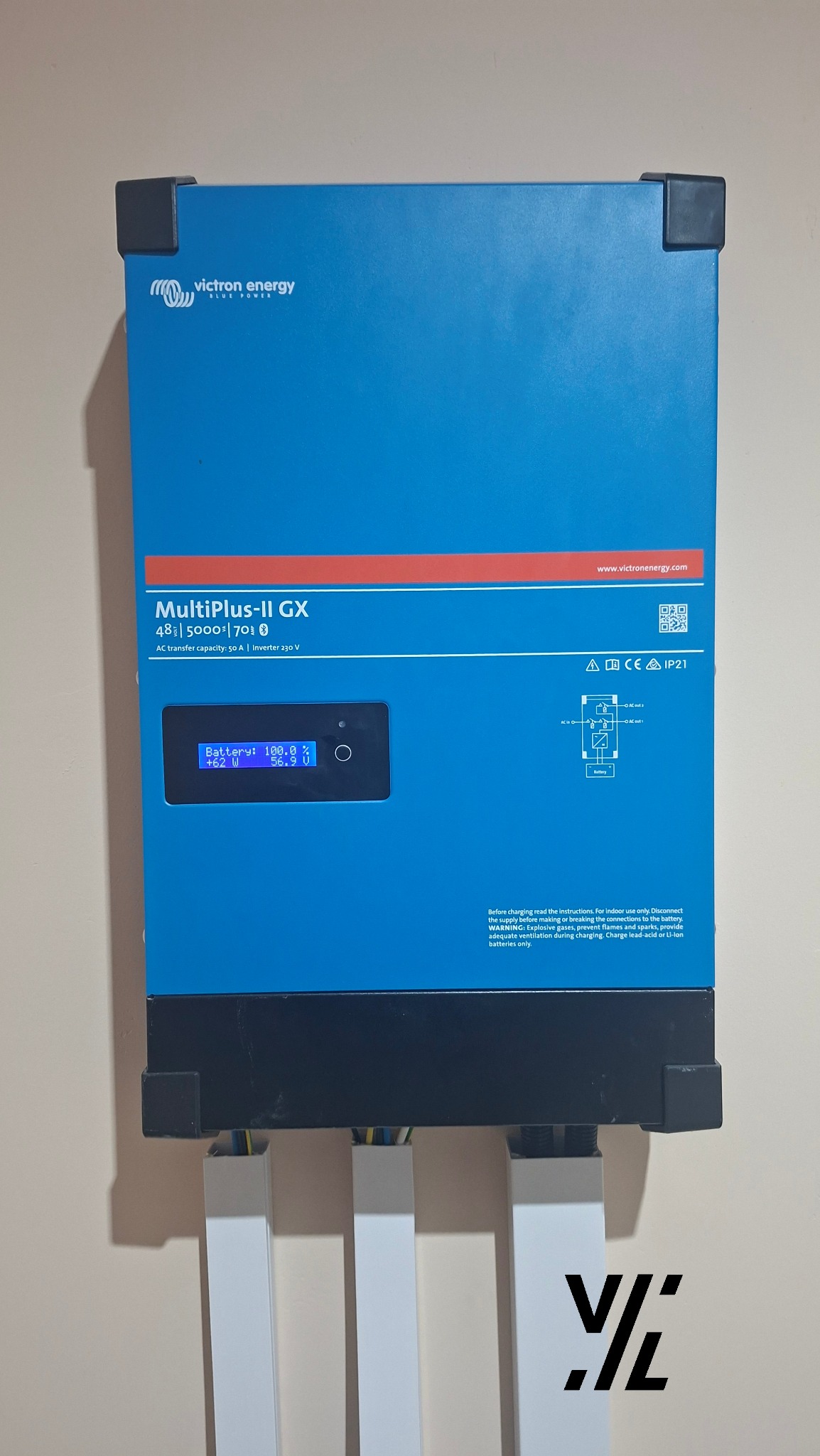 Niebieski inwerter hybrydowy Victron Energy MultiPlus-II GX zamontowany na ścianie, z widocznymi przewodami. Wyświetlacz LCD pokazuje parametry pracy.