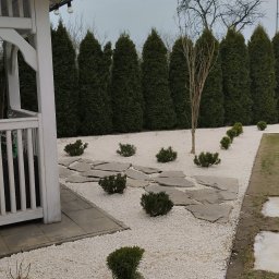 Finezja Katarzyna Olejarz - Minimalistyczny ogród po metamorfozie: białe kamienie, ścieżka z płyt, tuje i karłowate krzewy. Widoczny fragment białej altany. Ogród reprezentacyjny, mało wymagający.