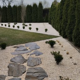 Finezja Katarzyna Olejarz - Ogród po metamorfozie: ścieżka z kamieni na białym żwirze, równo przycięte tuje i krzewy. Nowoczesna aranżacja przestrzeni.