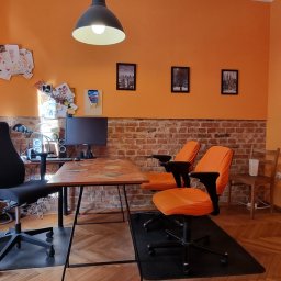 On The Hill - Pomarańczowy pokój z biurkiem ozdobionym naklejkami, monitor, krzesła biurowe i ściana z cegły. Na ścianie rysunki dziecięce i zdjęcia.