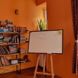 On The Hill - Pokój z pomarańczowymi ścianami, regał z książkami, tablica z napisem 'succeed', roślina w oknie i zasłona. Scena lekcji języka angielskiego.