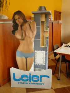 Wydruk UV: kartonowa figura kobiety w bieliźnie obok przekroju komina systemowego Leier, na jasnym tle.
