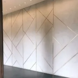 Ściana z mikrocementu w geometryczne wzory z metalicznymi listwami, oświetlona punktowo, z widoczną częścią ciemnej podłogi i zasłony w rogu.