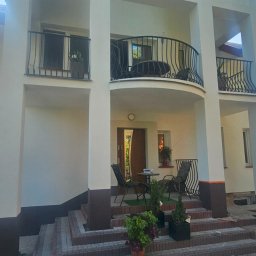 Budolix Paweł Wołoszyn - Odnowiona fasada domu z balkonem i kolumnami, widoczne detale wykończenia, schody wejściowe i elementy dekoracyjne. Jasna kolorystyka elewacji.