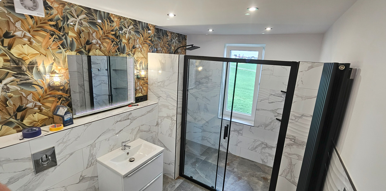 Nowoczesna łazienka z kabiną prysznicową typu walk-in, umywalką z szafką, lustrem z podświetleniem LED i grzejnikiem. Ściany wyłożone płytkami imitującymi marmur.