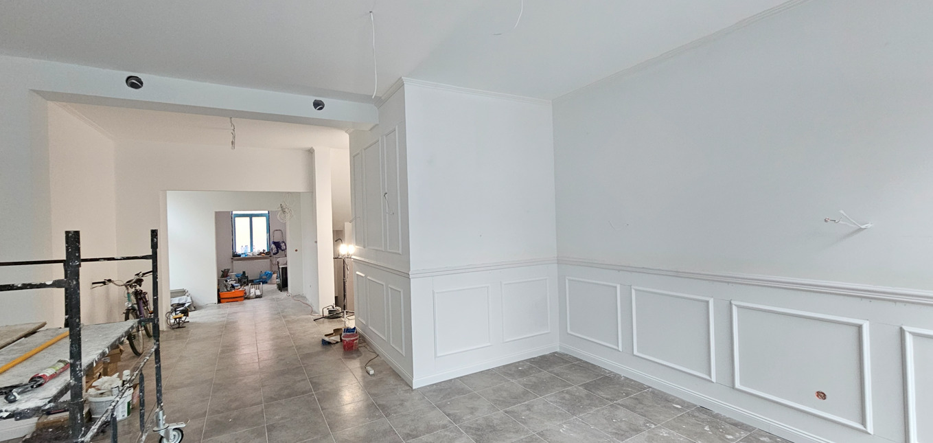 Białe ściany z dekoracyjnymi panelami w odnowionym wnętrzu. Widoczne rusztowania i narzędzia, co sugeruje trwający proces wykończeniowy.