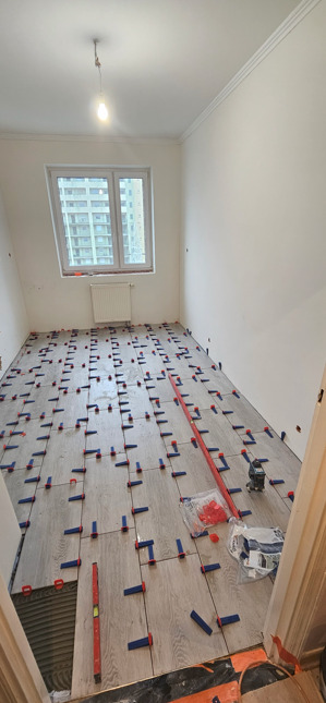 Układanie płytek podłogowych z użyciem poziomicy i lasera krzyżowego w Hrubieszowie. Widoczne klipsy i kliny do poziomowania płytek.