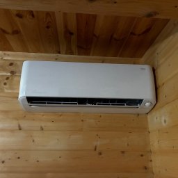 Wenturo Sp. z o. o. - Biała klimatyzacja ścienna zamontowana w drewnianym wnętrzu. Widoczny fragment sufitu z boazerii. Kątowe ujęcie z dołu.