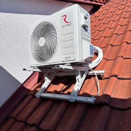 Wenturo Sp. z o. o. - Biała jednostka zewnętrzna klimatyzacji Rotenso zamontowana na dachu z czerwonej dachówki, widok z dołu na tle błękitnego nieba.
