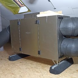 Wenturo Sp. z o. o. - Centrala rekuperacyjna z podłączonymi przewodami wentylacyjnymi, zainstalowana na poddaszu z drewnianą podłogą i widocznym oknem dachowym.