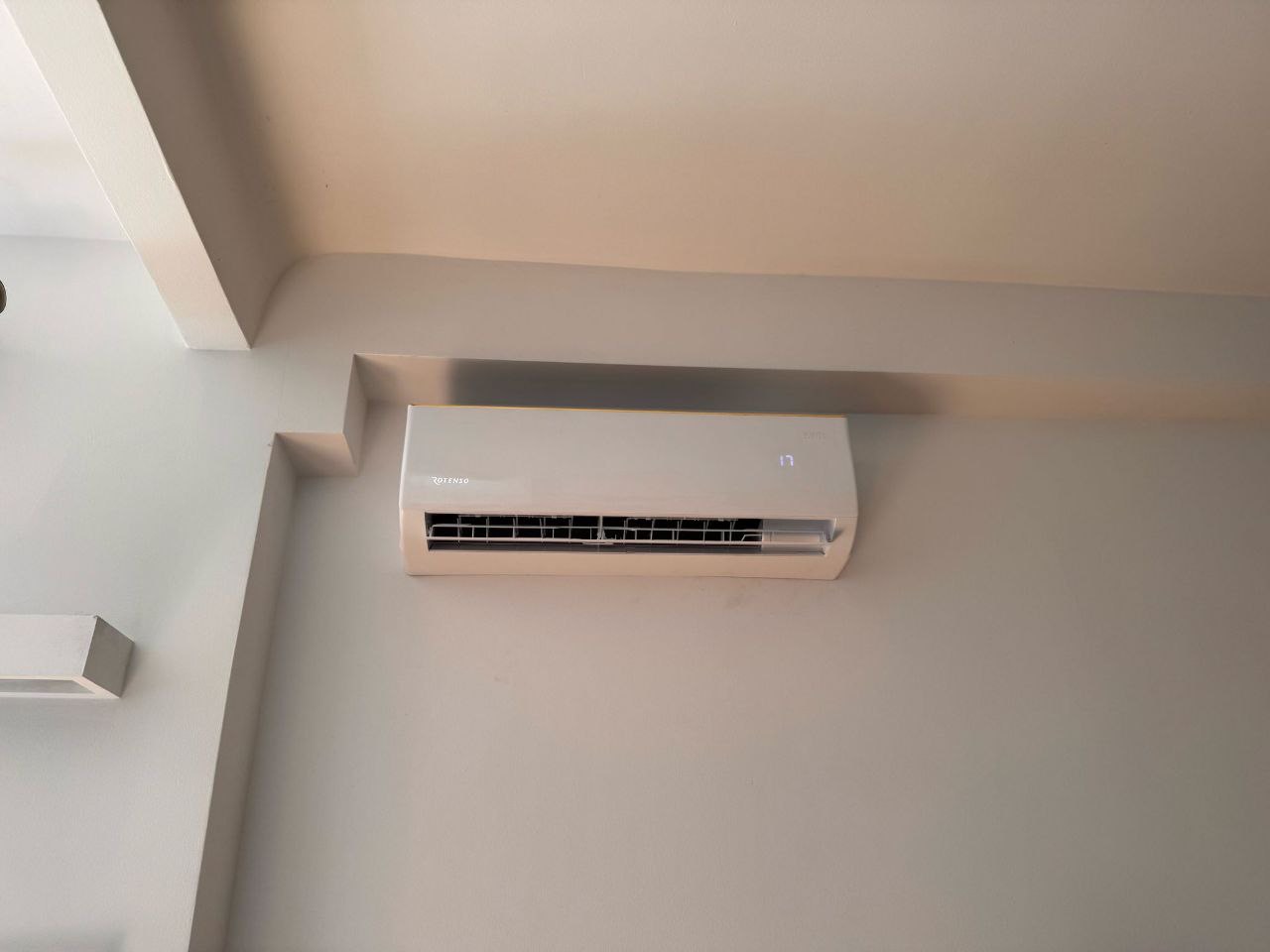 Biały klimatyzator Rotenso zamontowany na ścianie, widoczny wyświetlacz z temperaturą 17 stopni, minimalistyczny design, neutralne tło.