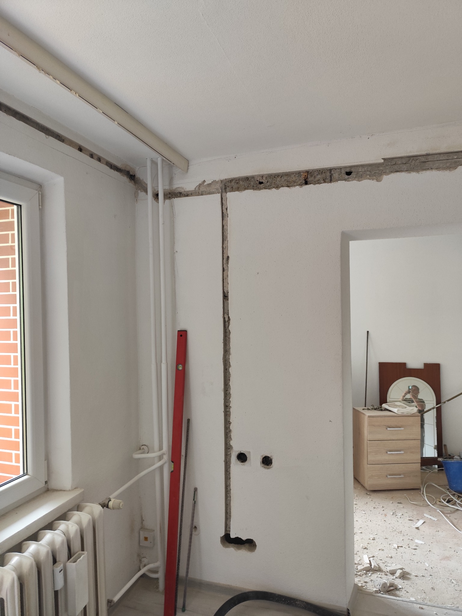 Remont pokoju: bruzdy w ścianie pod instalacje, widoczne rury, poziomica. Otwory pod gniazdka elektryczne. W tle bałagan po kuciu.