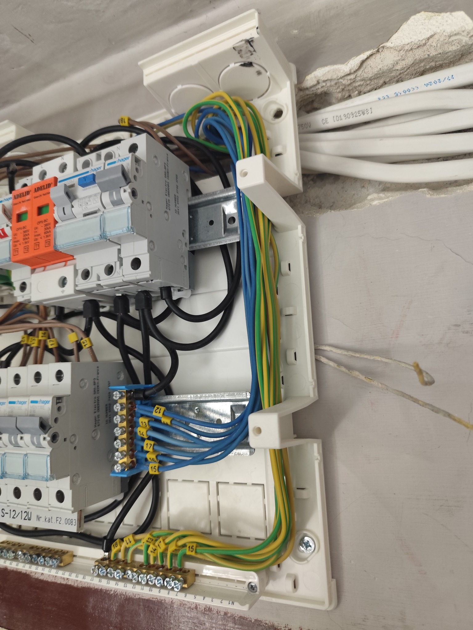 Rozdzielnica elektryczna Hager z podłączonymi przewodami oznaczonymi numerami, widoczne bezpieczniki i listwy zaciskowe. Instalacja wewnątrz budynku.