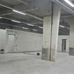 Wnętrze hali w trakcie budowy ścian działowych z betonu komórkowego. Widoczne surowe słupy i instalacja oświetleniowa pod stropem. Na podłodze widoczny odkurzacz.